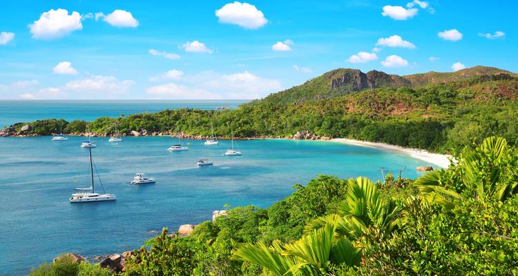 Panoramische Bucht mit azurblauem Wasser und ankernden Yachten, eingerahmt von üppigen tropischen Hügeln auf der Insel Praslin.