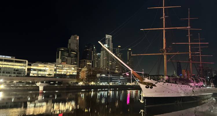 Elegant groot zeilschip met hoge masten aangemeerd op een spiegelglad rivier met 's nachts verlichte wolkenkrabbers van Buenos Aires.
