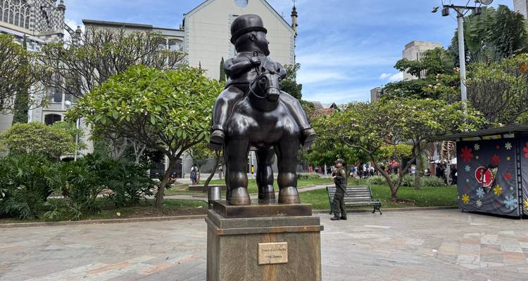Bronzen Botero-standbeeld van een man op een paard in een groene openbare plein in Medellín.