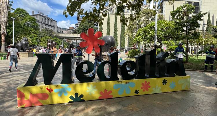 Kleurrijke 'Medellín' bord op een stadsplein omgeven door bezoekers en openbare kunstsculpturen.