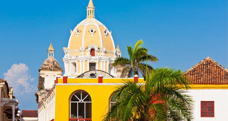 Een felgeel koloniaal gebouw en palmboom omlijsten de beroemde kathedraalkoepel onder een heldere blauwe Cartagena-hemel.