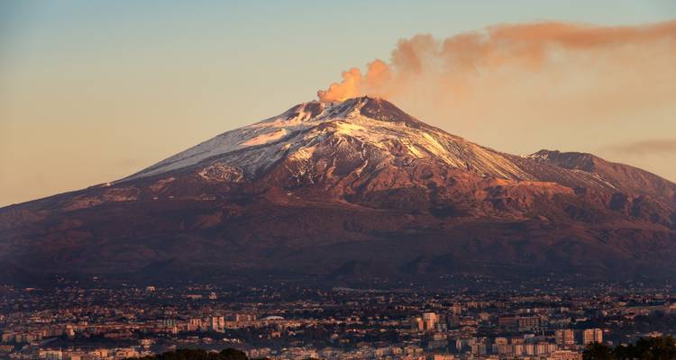 Sneeuwbedekte Mount Etna die tijdens zonsopgang een rookpluim boven de stad Catania uitstoot.