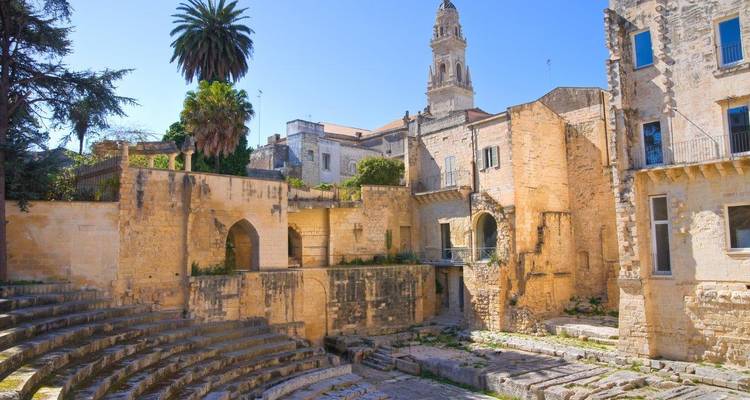 Ruïnes van een oud Romeins amfitheater in Lecce verlicht door warm zonlicht met een klokkentoren die erachter uittorent.