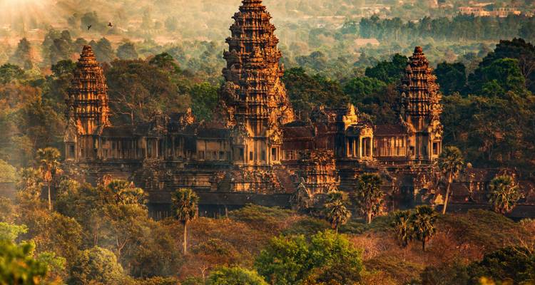 Aerial view of Angkor Wat’s stone towers rising above dense Cambodian forest bathed in warm morning light.