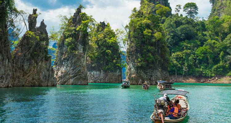 Les bateaux à longue queue glissent dans une eau d'émeraude entourée de pic de calcaire imposants à Khao Sok.