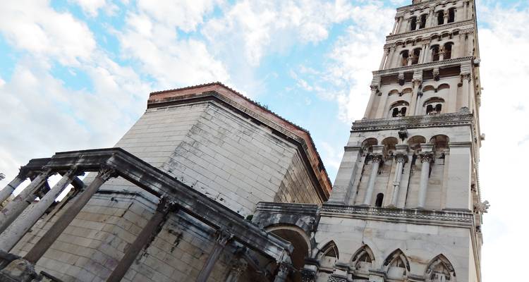 Opwaartse weergave van de klokkentoren van de Kathedraal van Split en aangrenzende bogen tegen een gedeeltelijk bewolkte hemel.