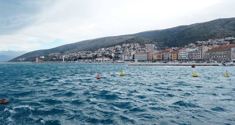 Golvend blauw water op de voorgrond met een Kroatisch kuststadje en bergen erachter.