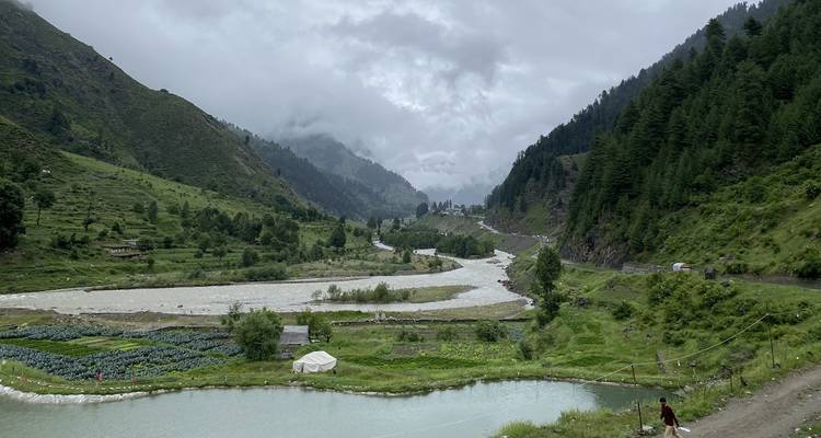 Neblige Bergtallandschaft mit Fluss, Gemüsefeldern und einem kleinen Zelt neben einem spiegelnden Teich in Nordpakistan.