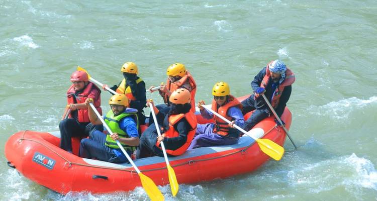 Ein Team von Wildwasser-Fahrern in Helmen und Schwimmwesten, die ein aufblasbares Boot durch schnell fließendes Flusswasser paddeln.