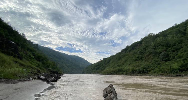 Ein breiter Fluss, der zwischen üppig grünen Hügeln unter einem teilweise bewölkten Himmel fließt.