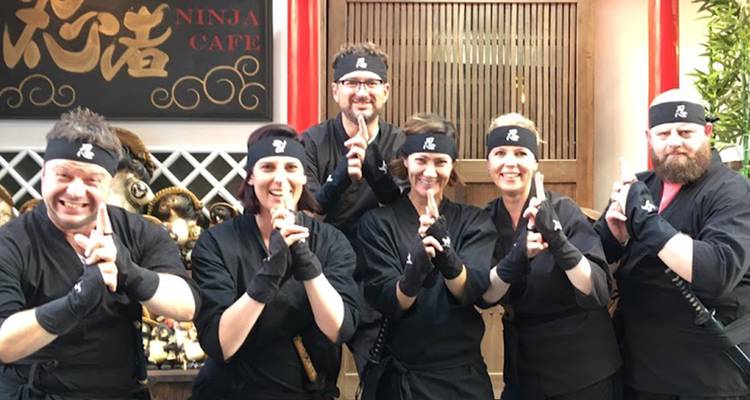 Eine Gruppe in schwarzen Ninja-Kostümen, die verspielt in einem thematisierten Café posiert.