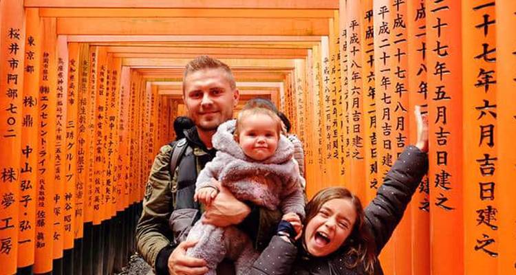 Ein Vater, der ein Baby hält, und ein lachendes Kind im Inneren des karminroten Torii-Tunnels des Fushimi-Inari-Schreins.