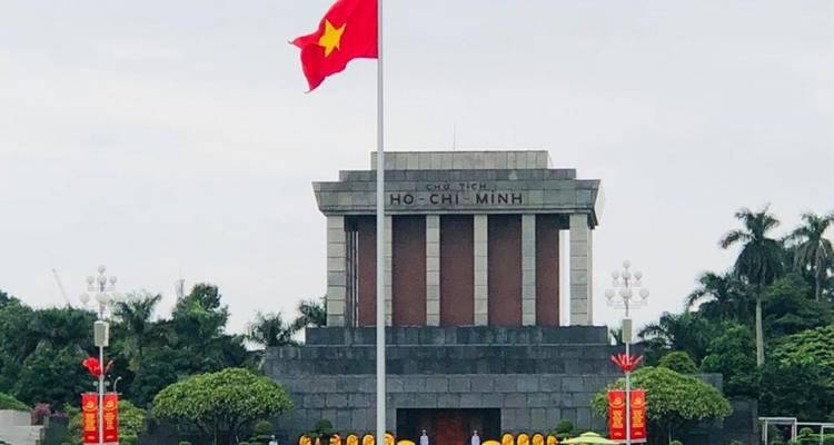 Front view of Ho Chi Minh Mausoleum with Vietnam flag flying high on a cloudy day.