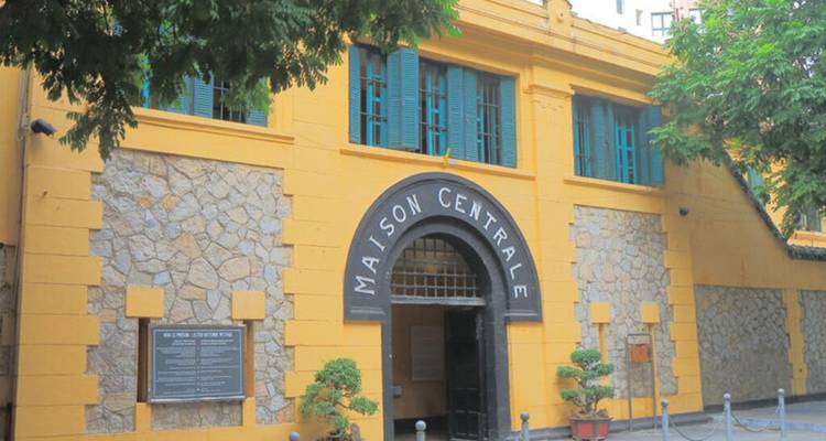 Yellow stone façade of historic Maison Centrale prison with arched entrance in Hanoi.