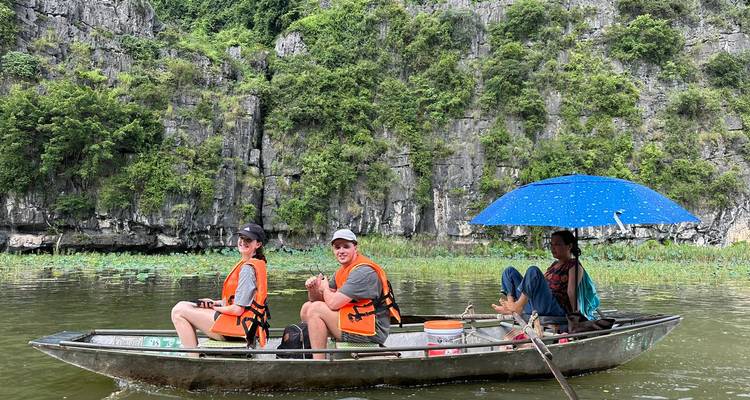 Small metal boat glides past limestone cliff while rower shelters under blue umbrella.