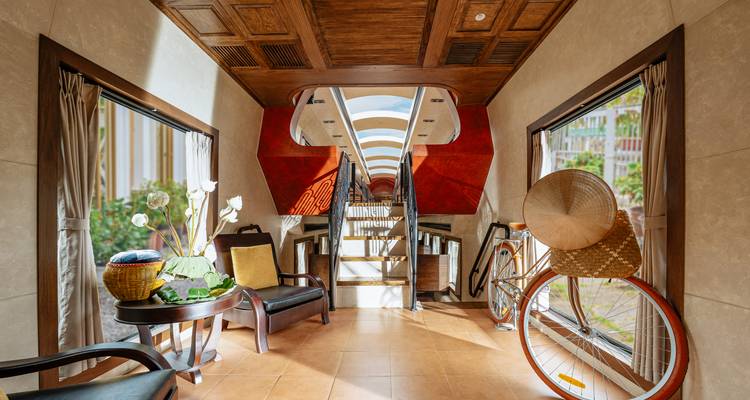 Stilvoller Loungebereich in einem luxuriösen Zugwagen mit großen Fenstern, Holzdecke und vietnamesischer Dekoration.