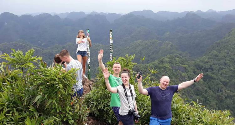 Excursionistas felices saludando desde una estrecha cresta de montaña rodeada de picos de karst verde.