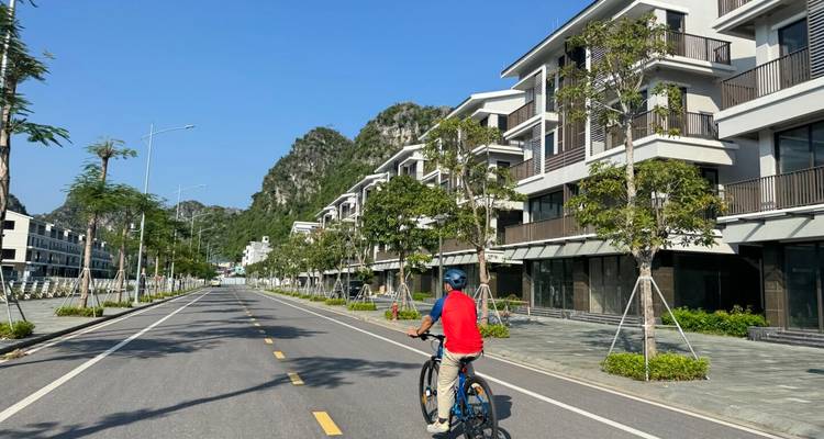 Un ciclista solitario pedalea por un bulevar flamante con edificios modernos y colinas de karst a lo lejos.