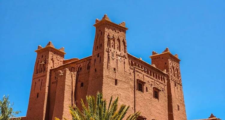 Zonbeschenen adobe kasbah met sierlijke torens tegen een diepblauwe hemel in Zuid-Marokko.