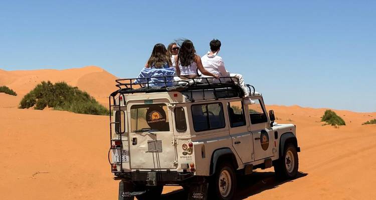 4 reizigers op het dak van een 4x4 Land Rover terwijl ze over gouden zandduinen in de Sahara rijden