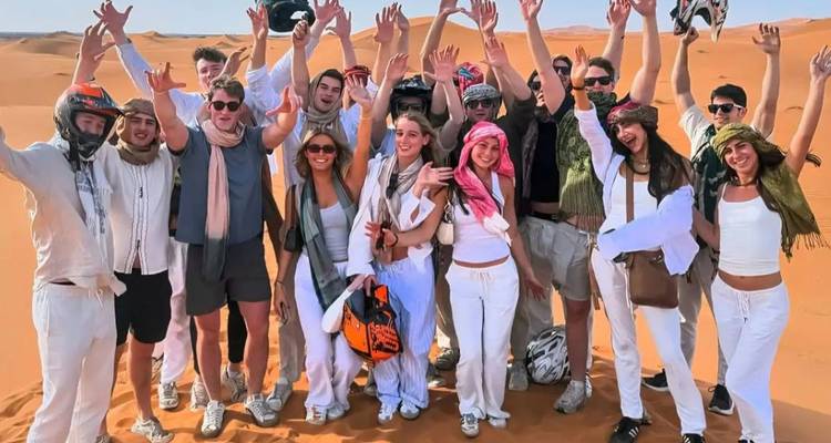 Grote toeristengroep in witte kleding viert feest met omhoog geheven handen op zandduinen
