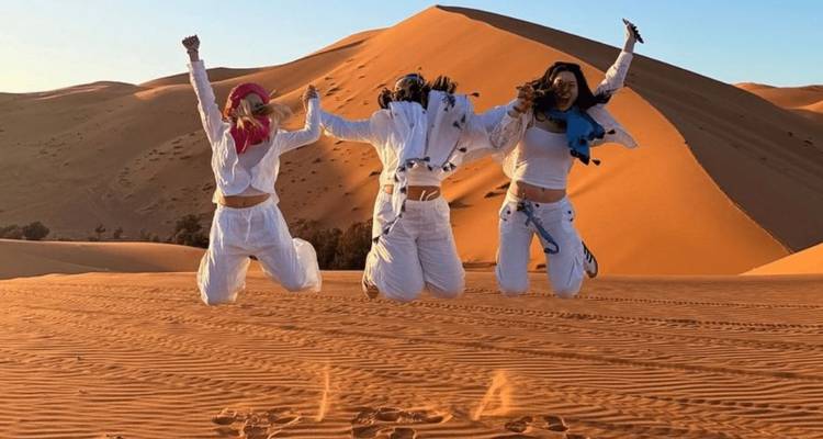 Drie reizigers die tegelijkertijd springen op gloeiend zand in de woestijn tijdens zonsondergang