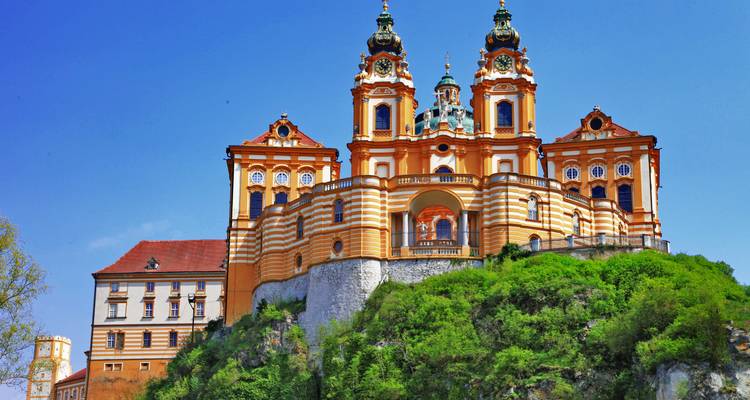 L'abbaye baroque de Melk perchée sur un promontoire rocheux avec sa façade orange vif et la végétation luxuriante en contrebas.
