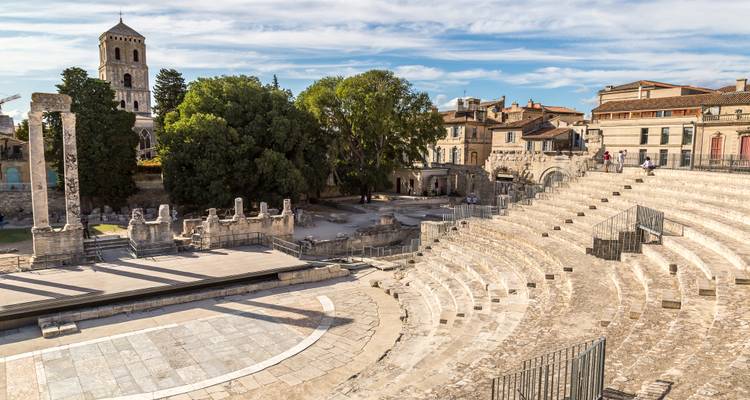 Ruins of the Roman theatre in Arles with stone seating curves and ancient columns under a bright sky.