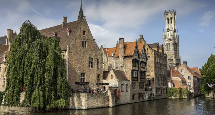 Scène médiévale de canal avec maisons en pierre et le Beffroi s'élevant au-dessus dans un ciel dégagé.
