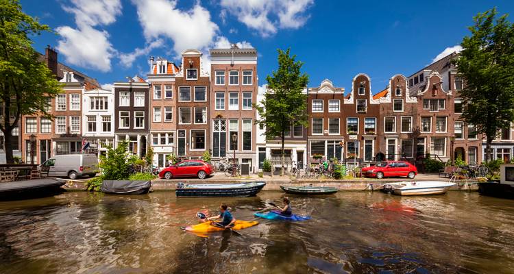 Les kayakistes pagaient le long d'un canal d'Amsterdam bordé de grandes maisons de canal sous un ciel bleu éclatant.