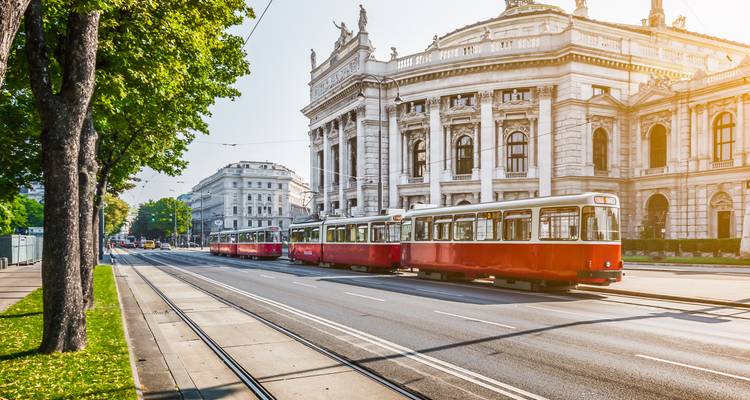 Les tramways rouges classiques passant devant le majestueux Burgtheater de Vienne par une belle matinée ensoleillée.