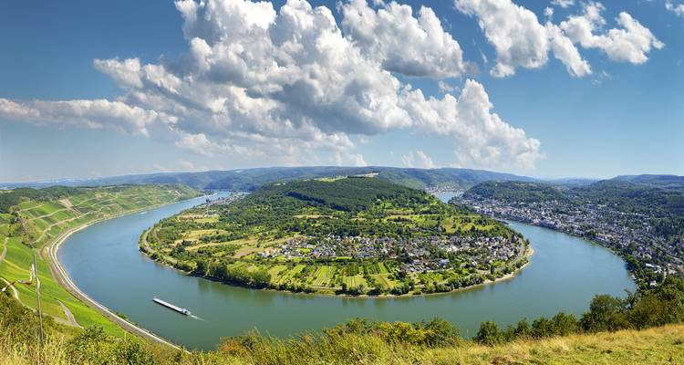Vue aérienne large d'un virage spectaculaire du Rhin entouré de vignobles verdoyants et de villes sous des ciels bleus.
