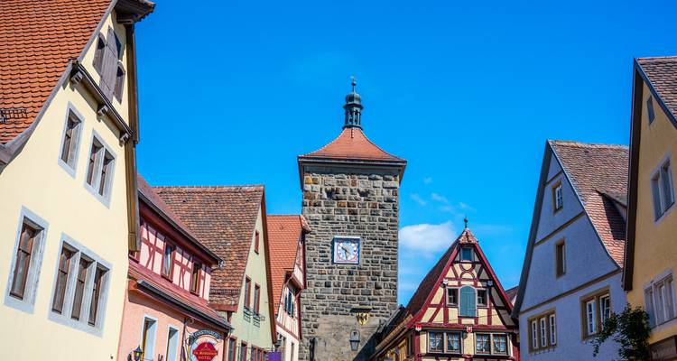 Casas de entramado de madera coloridas y una torre de piedra con reloj en Rothenburg ob der Tauber contra un cielo azul brillante.