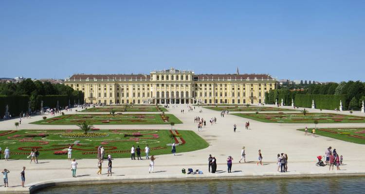 De vastes jardins formels mènent à la majestueuse façade jaune du Palais de Schönbrunn de Vienne, parsemée de visiteurs en promenade.