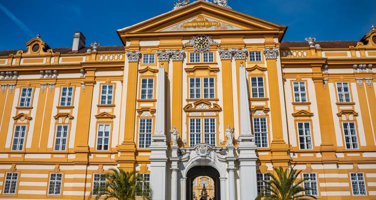 Façade jaune vif et blanche de l'abbaye de Melk avec ornementation baroque sur un ciel bleu