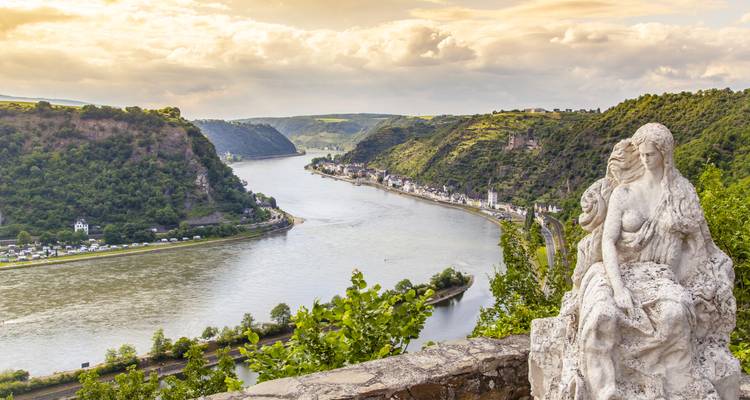 Vue panoramique des Gorges du Rhin depuis un belvédère élevé avec une statue au premier plan et le fleuve sinueux en contrebas.