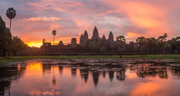 Angkor Wat silhouette mirrored in lotus pond at vibrant orange sunrise.