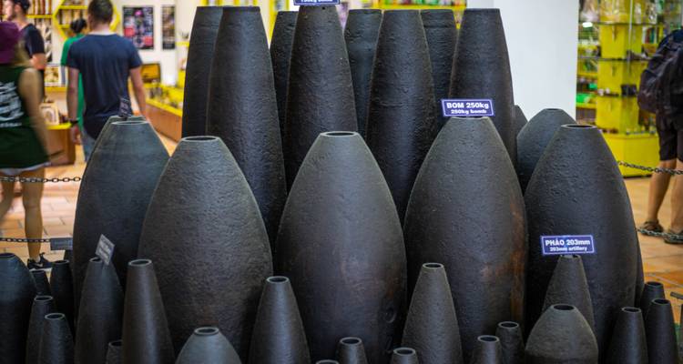 Exhibit of dark bomb shells displayed in War Remnants Museum with visitors browsing in background.