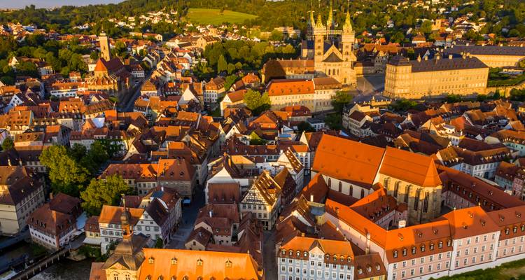 Gouden-uur luchtfoto van een roodgedekt middeleeuws stadje met een indrukwekkende kathedraal met twee torens en paleizencomplex, omringd door groen.