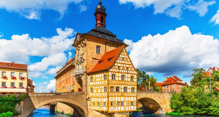 Het vakwerkgebouw Altes Rathaus van Bamberg thront boven een stenen brug tegen een helder blauwe lucht en witte wolken.