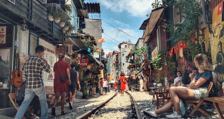 Escena callejera vibrante en la famosa Train Street de Hanói con cafés, peatones y vías de tren en el medio.