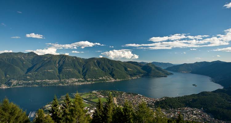 Point de vue élevé surplombant un vaste lac alpin entouré de montagnes verdoyantes accidentées sous un ciel dégagé.