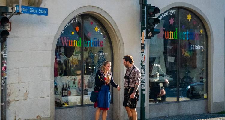 Un couple vêtu de manière décontractée discute devant une boutique sur une étroite rue allemande, des étoiles colorées ornant les vitrines.