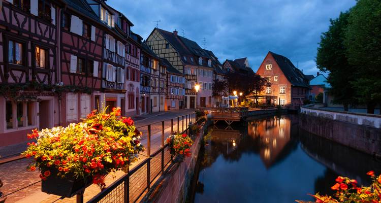 Le crépuscule s'installe sur le canal de Colmar bordé de jardinières fleuries et de maisons alsaciennes à colombages illuminées.