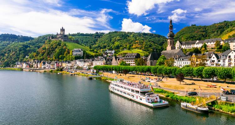 Un bateau de croisière fluviale s'approchant d'une charmante ville de la vallée de la Moselle dominée par le château de Reichsburg perché sur la colline
