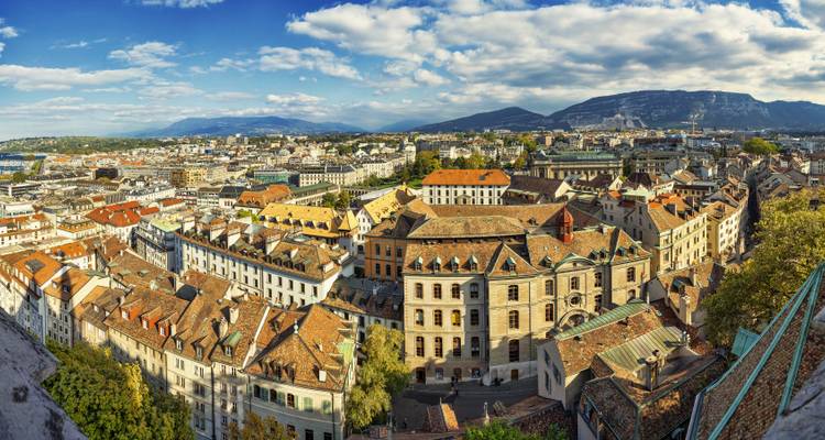 Vue panoramique en plongée sur les toits en tuiles de Genève avec des montagnes lointaines sous des nuages épars