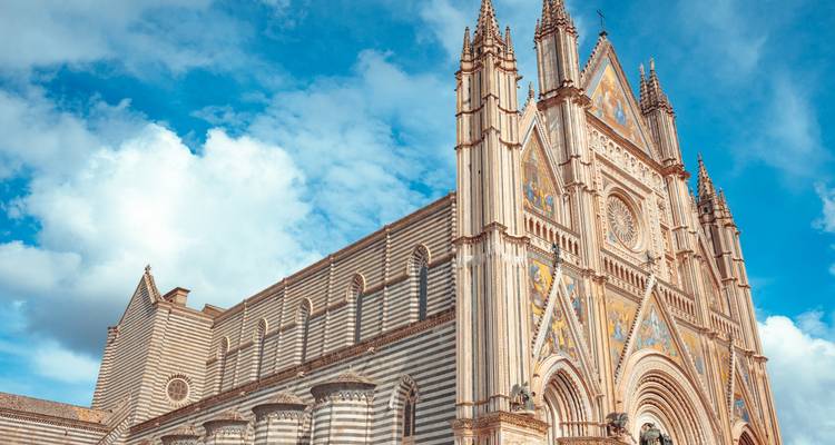 Façade rayée magnifique de la Cathédrale d'Orvieto s'élevant dans un ciel bleu clair avec des nuages floconneux.