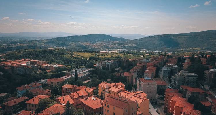 Vue aérienne d'une ville italienne moderne construite sur les collines, avec des toits en tuiles rouges s'étendant sur le terrain vallonné.