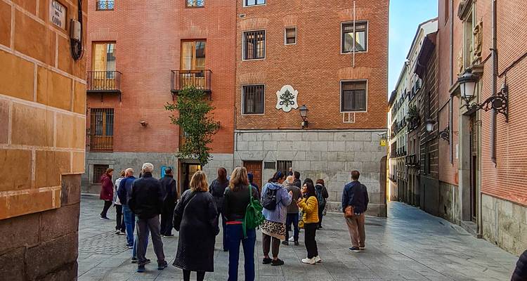 Grupo de tour a pie guiado escuchando a un guía en un callejón estrecho de ladrillos del Madrid histórico.