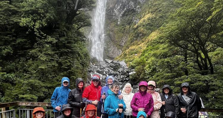 Grote wandelgroep in kleurrijke regenkleding poseert voor een hoge waterval in weelderig bos.